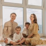 A cheerful family of four sitting together on the floor of a sunlit living room.